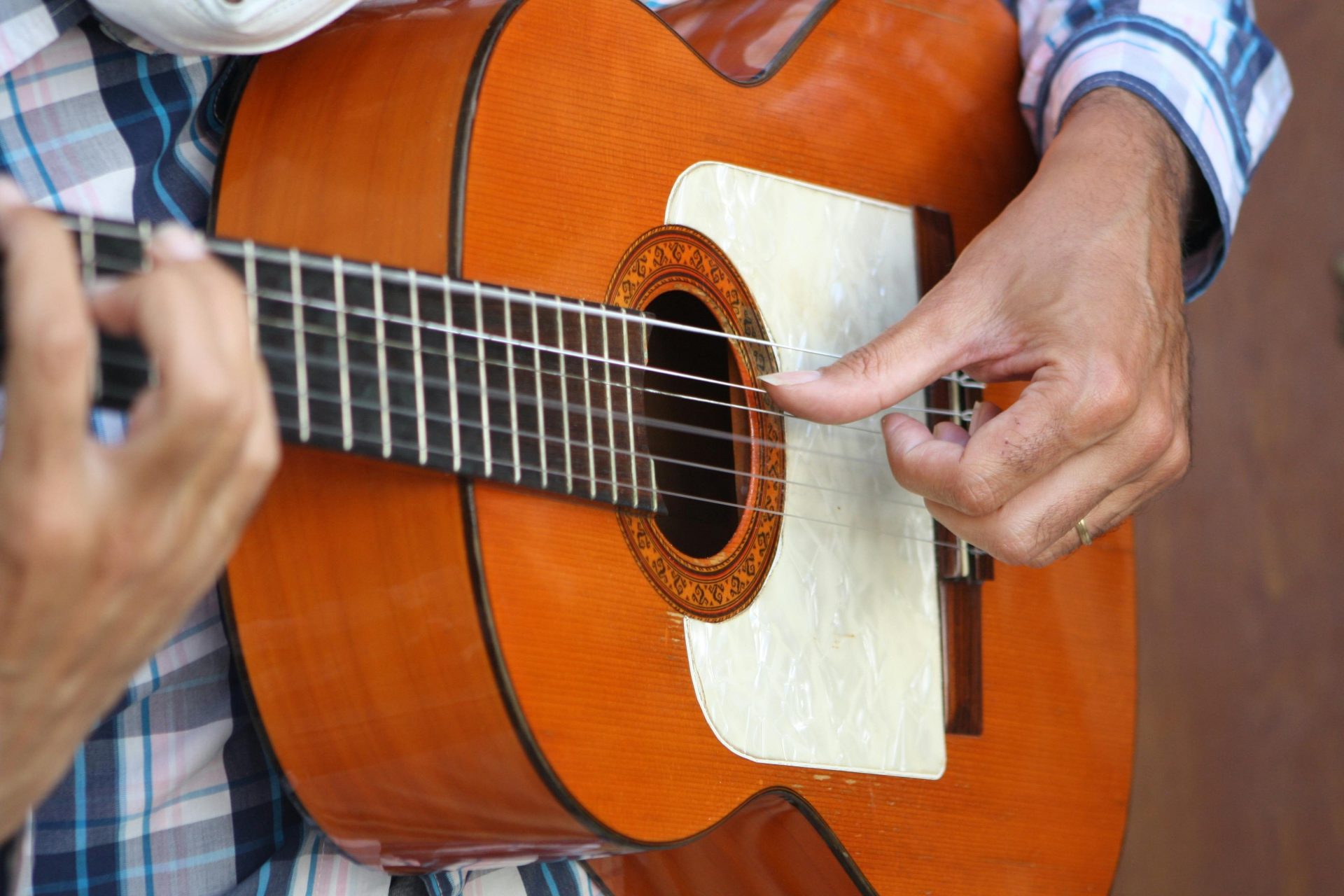 Un primer plano detallado de las manos de un guitarrista flamenco rasgueando una guitarra de madera en Córdoba, España.