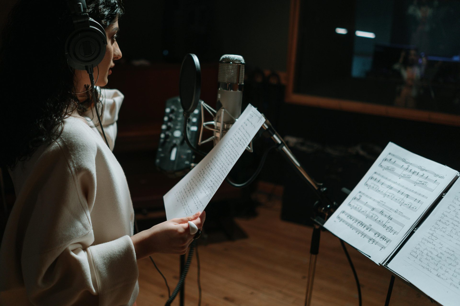 Mujer en un estudio de música grabando una canción con un micrófono de condensador y auriculares.
